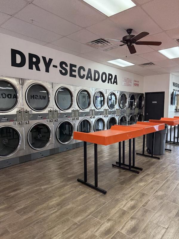 Stacked dryers under a Dry-Secadora sign with orange folding tables at a Rock Hill laundromat